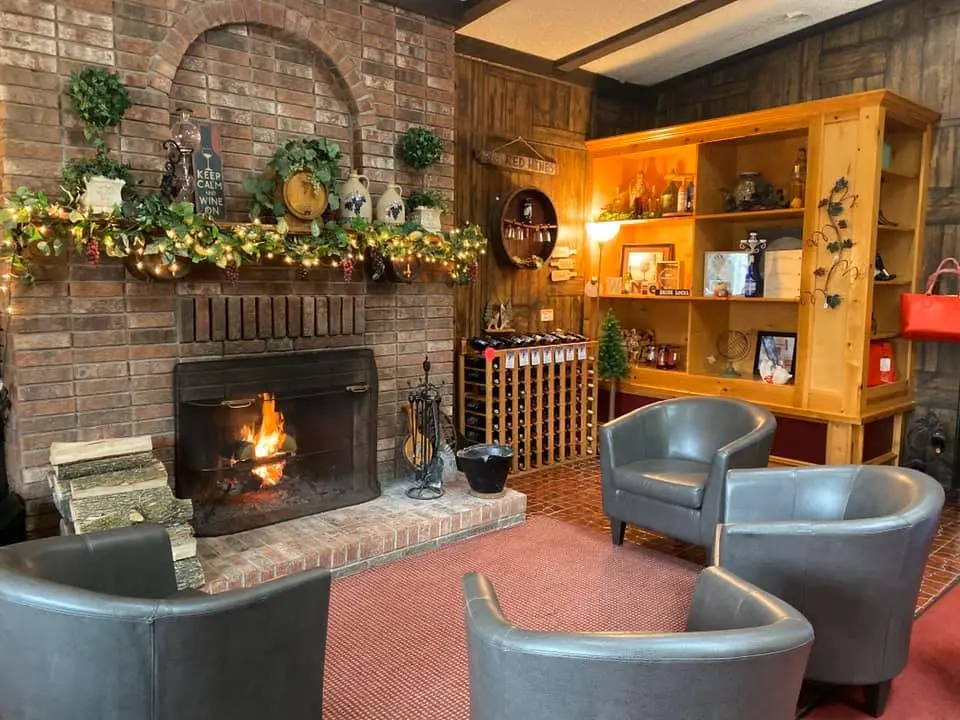 Cozy winery lounge with brick fireplace, decorated mantle, wine rack, and comfortable seating